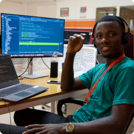A young man behind a desktop and a laptop programming